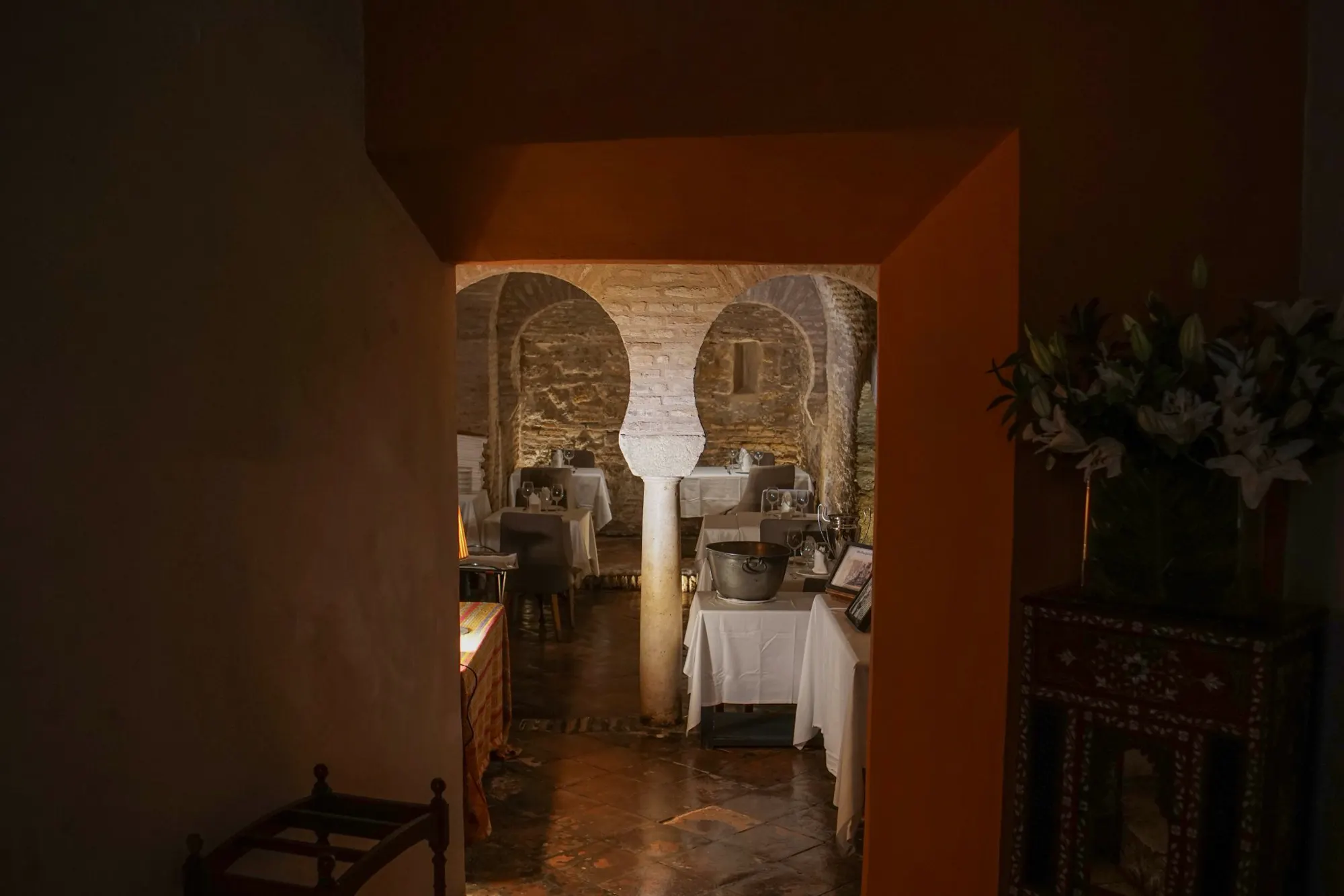 Tables laid with white cloths under brick arches in a dimly lit cellar