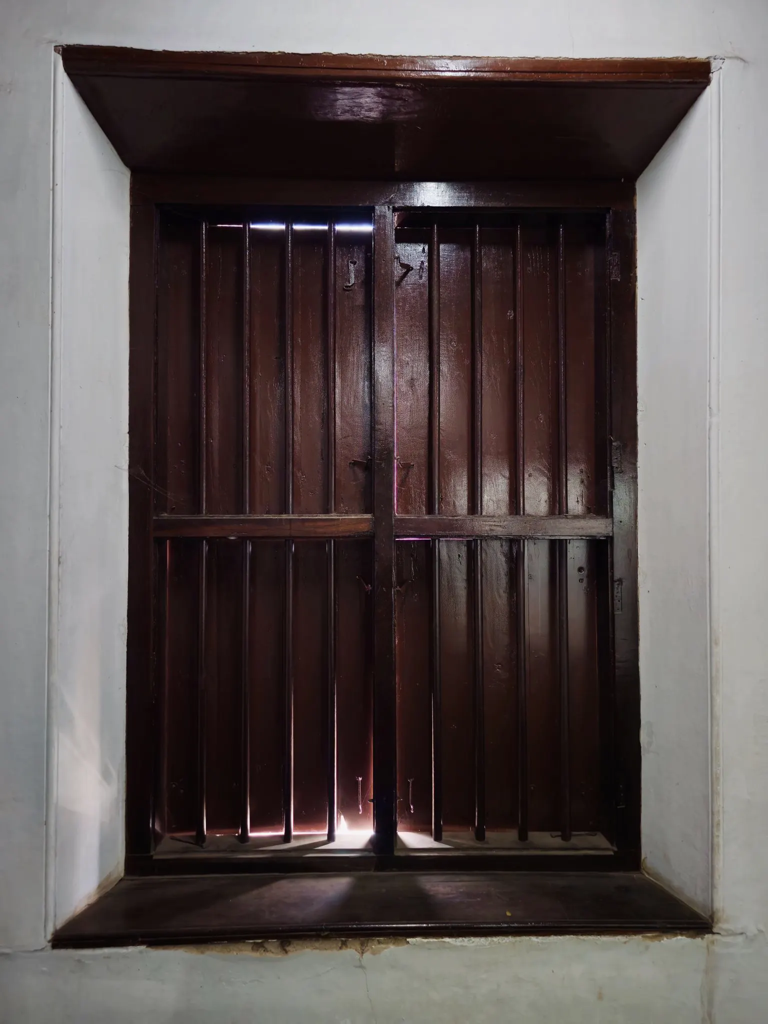 Dark wooden shutters closed over a deep window, daylight showing between them