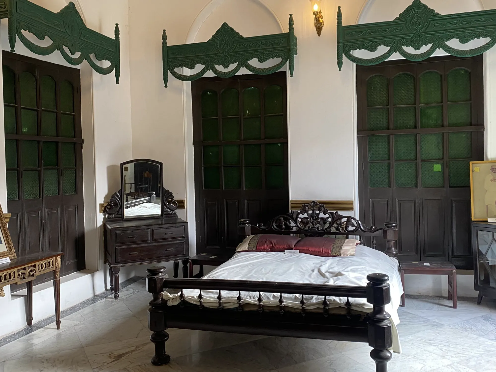 A bedroom with a carved wooden bed and two tall green doors onto a balcony