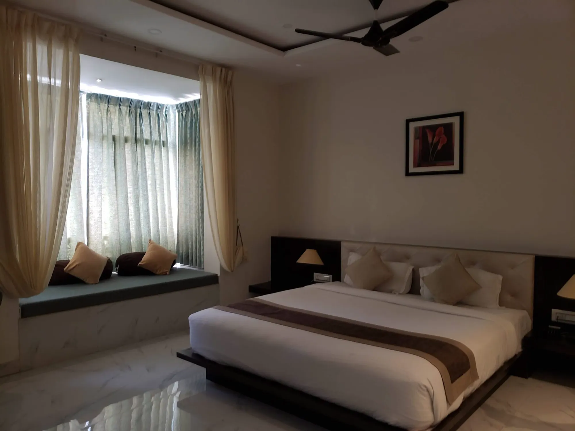 A bright bedroom with a deep cushioned window seat under sheer curtains