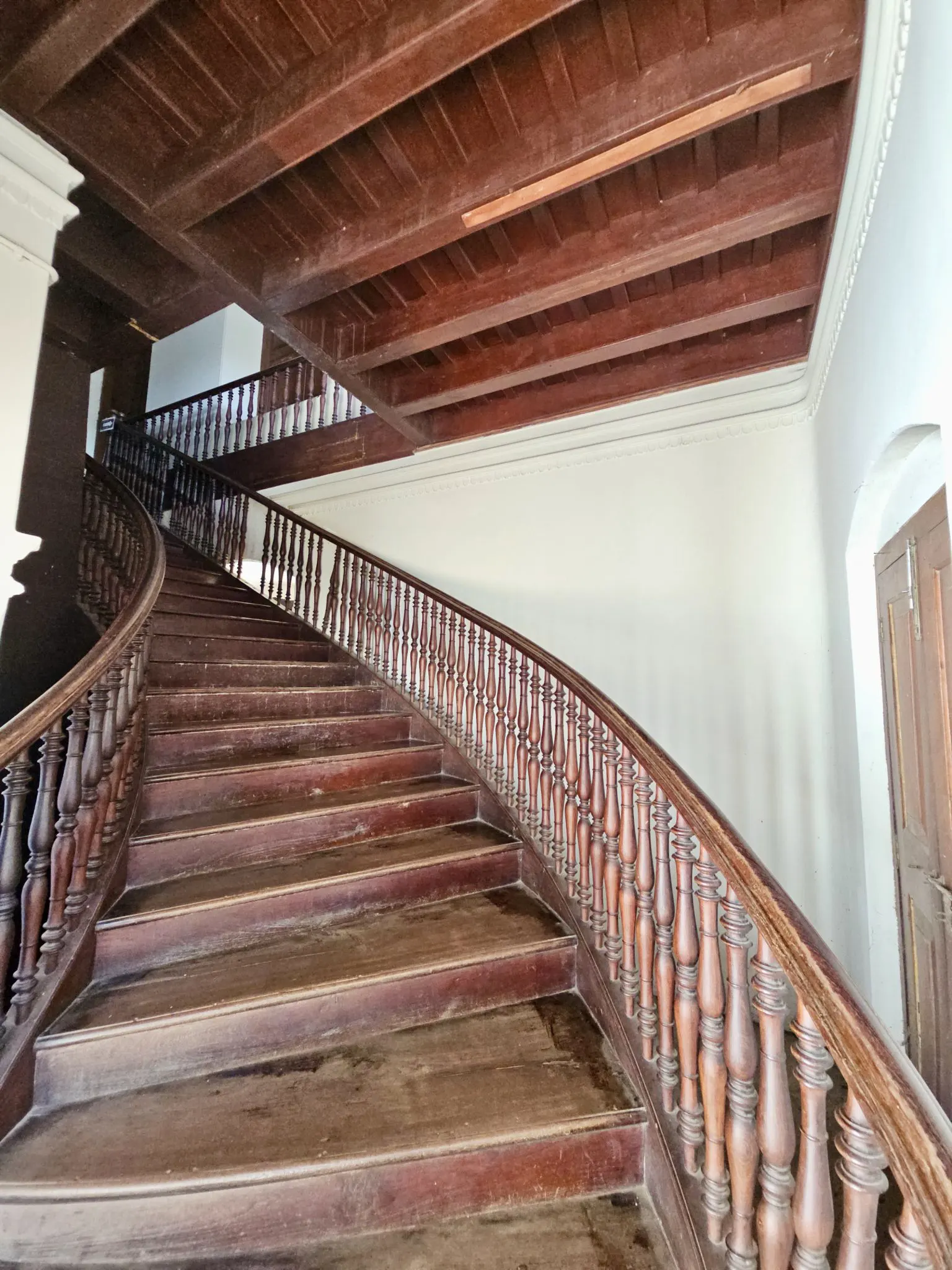 A wooden staircase with carved handrails curving up under a beamed ceiling
