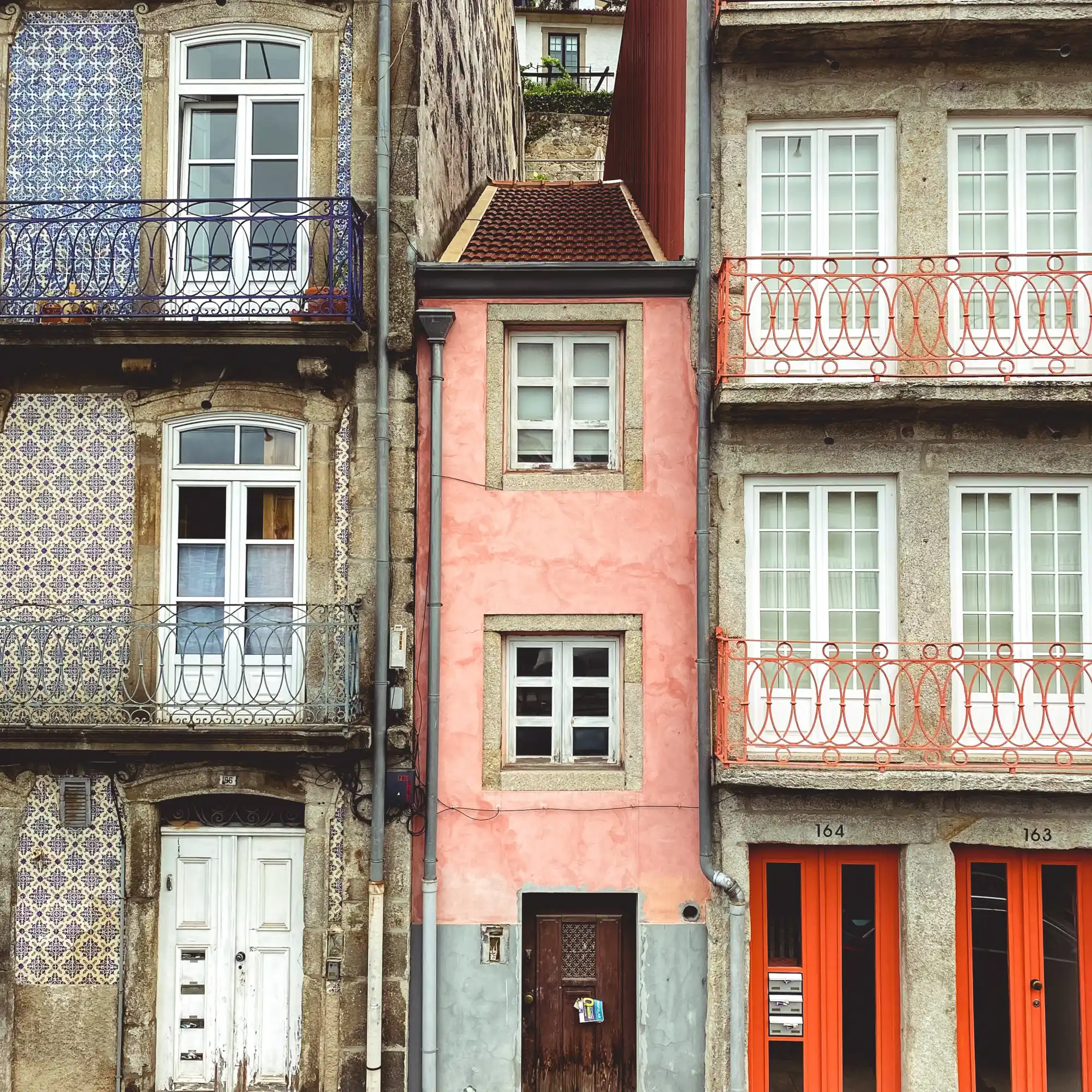 Tiled townhouses with iron balconies across a narrow Porto street