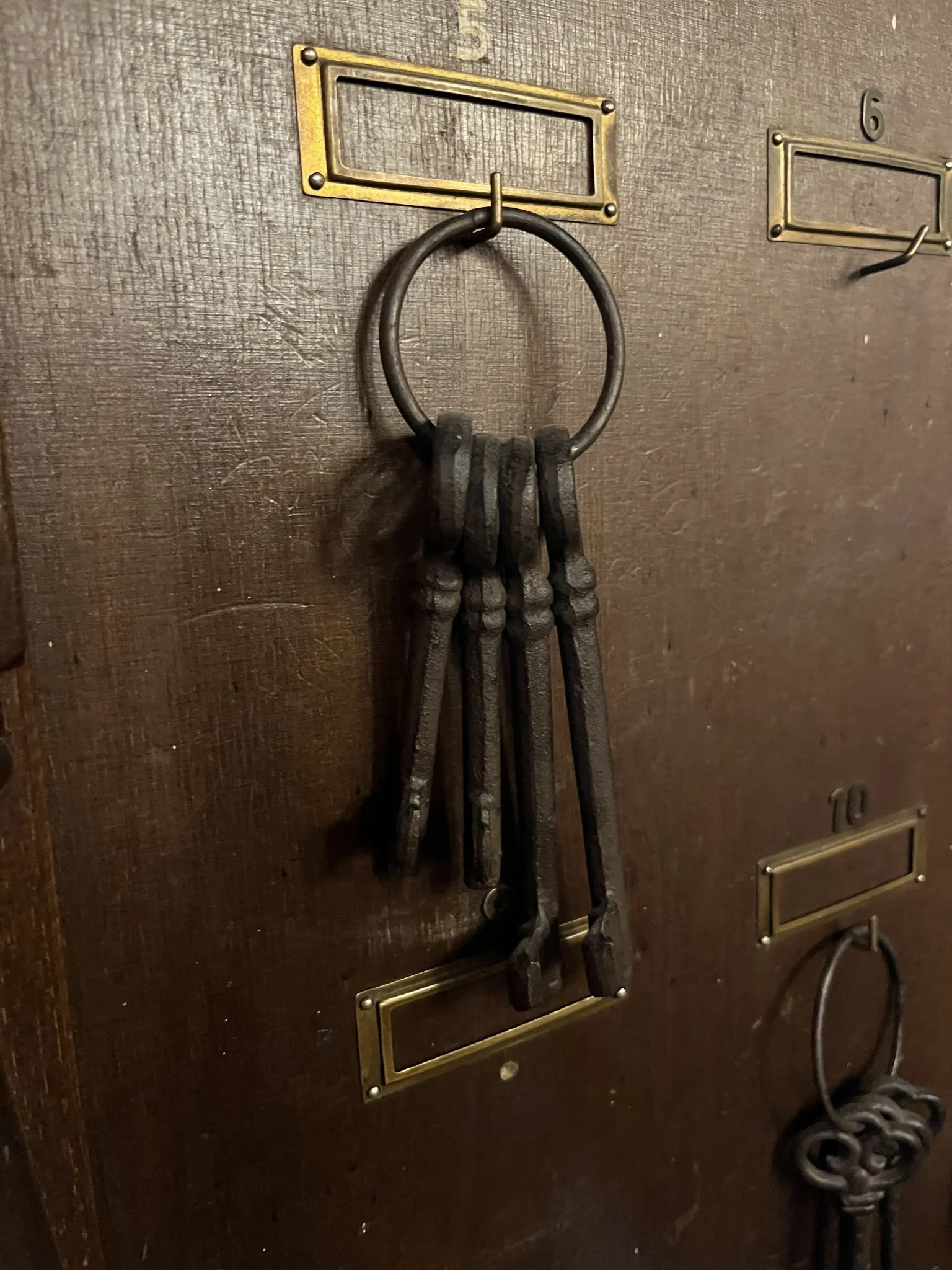 Old iron room keys hanging from brass hooks on a wooden board